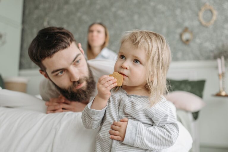 A loving father watches his baby daughter enjoying a snack at home. Warm and tender family moment.